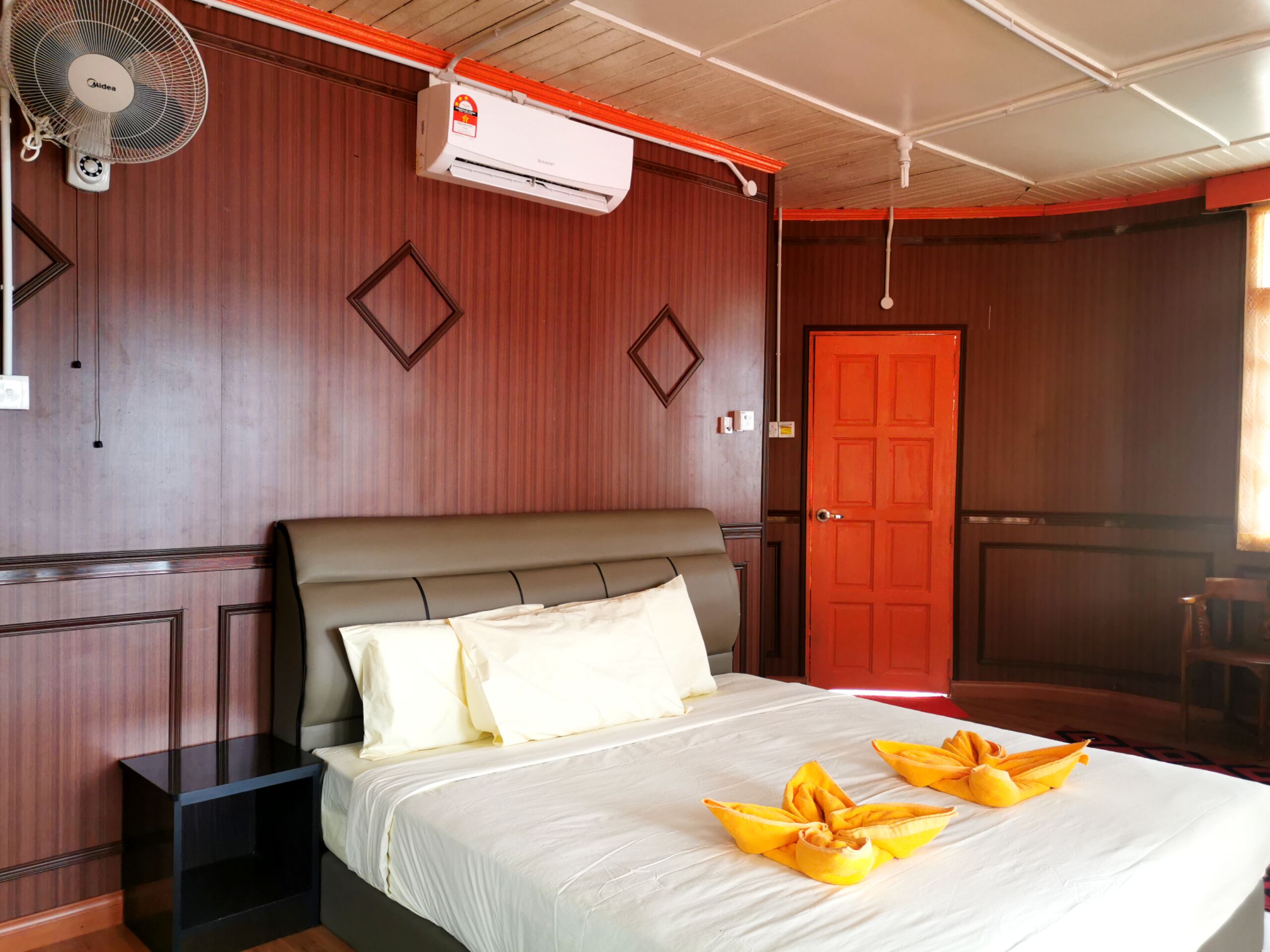Une chambre d’hôtel comprenant un lit, une table de chevet, un appareil de climatisation et un mur en bois orné de panneaux décoratifs.