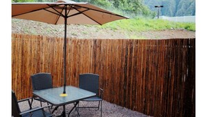 Un patio con una mesa, sillas, una sombrilla grande y una cerca de bambú.