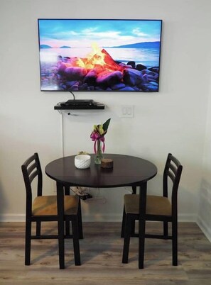 Een eetgedeelte met een ronde tafel, twee stoelen, een flatscreen televisie aan de muur en een klein plantje op tafel.