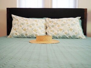 Un lit avec un panier en osier et deux oreillers ornés d’un motif représentant des coquillages et des étoiles de mer.