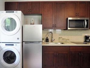 Een praktische keuken met een wasmachine, een koelkast, een magnetron en houten kastjes.