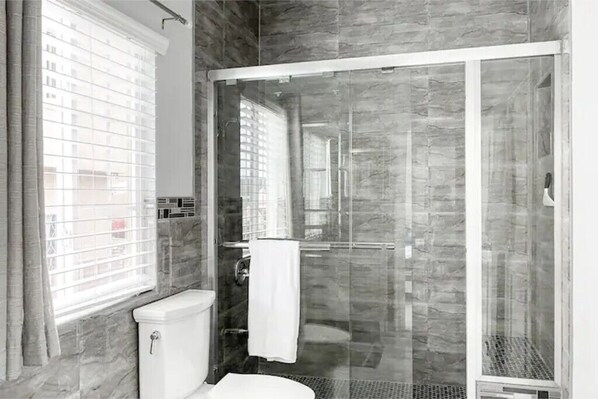 A modern bathroom with a glass shower enclosure, a toilet, and a window with blinds. - Airy Escape Ocho Rios, Spacious 3 BR, Central to attractions, Gated Community. (Ocho Rios)