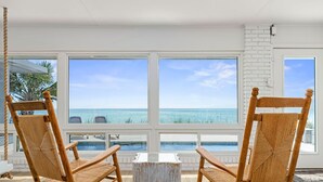 Quarto com duas cadeiras de vime voltadas para uma janela ampla com vista para a praia e o oceano.