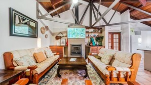 Un salon spacieux avec un plafond haut, des poutres apparentes, une cheminée et un téléviseur.