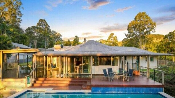 Une maison moderne dotée d’une piscine, d’un patio couvert et offrant une vue sur les arbres environnants.
