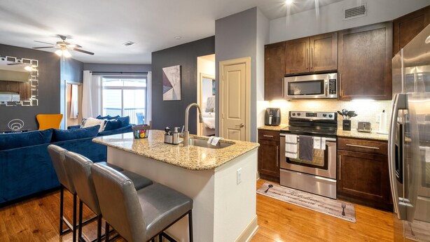 A modern kitchen with granite countertops, stainless steel appliances, and wooden cabinets. - A Touch of Class | MD Anderson/NRG (Houston)