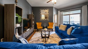 A living room with a blue sofa, a glass coffee table, and a ceiling fan. - A Touch of Class | MD Anderson/NRG (Houston)