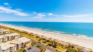 A coastal view with a beach, ocean, and a row of buildings with parking and greenery. - Ocean Forest Plaza 1911 (Myrtle Beach)