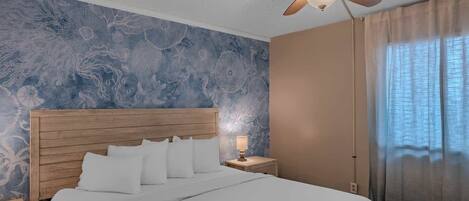 A bedroom with a wooden headboard, a bed with white bedding, a nightstand with a lamp, and a ceiling fan.