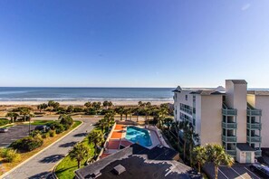 A hotel with a pool, a beach view, and a parking lot.