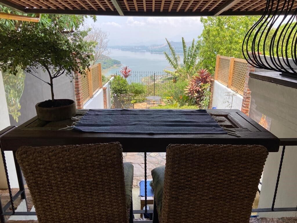 Un balcon avec des fauteuils en osier, une table et une vue sur un lac et des montagnes.