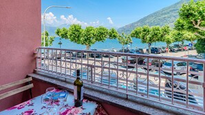 A balcony with a table set for two, overlooking a parking area and a body of water with trees and mountains in the background.
