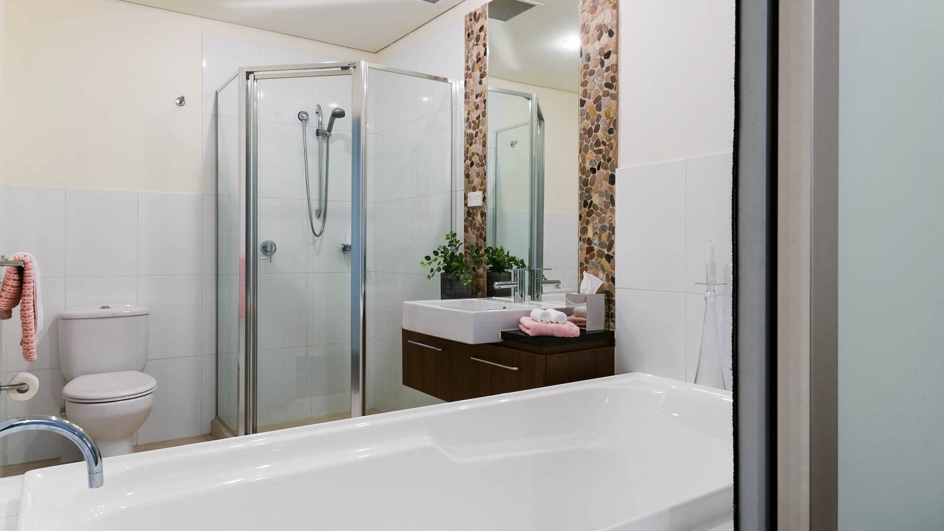 A modern bathroom with a glass-enclosed shower, a white bathtub, and a vanity with a mirror.