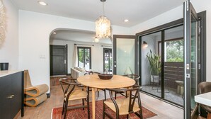 A dining area with a round table, chairs, and a chandelier. There is a sliding glass door leading to a balcony with a plant. - Bright Spanish Home in Prime LA Location (Los Angeles)
