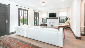A modern living room with a white sofa, a fireplace, a television, and a large window. - Bright Spanish Home in Prime LA Location (Los Angeles)