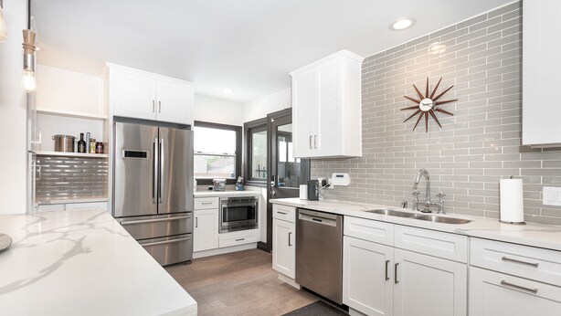A modern kitchen with white cabinetry, stainless steel appliances, and a gray brick backsplash. - Bright Spanish Home in Prime LA Location (Los Angeles)