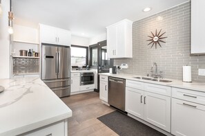 A modern kitchen with white cabinetry, stainless steel appliances, and a gray brick backsplash.