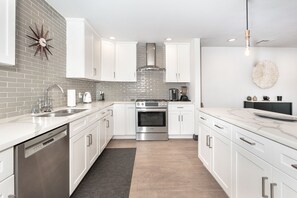 A modern kitchen with white cabinets, stainless steel appliances, and a brick backsplash. - Bright Spanish Home in Prime LA Location (Los Angeles)