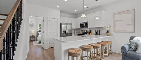 A modern kitchen with white cabinetry, stainless steel appliances, and a central island with stools.