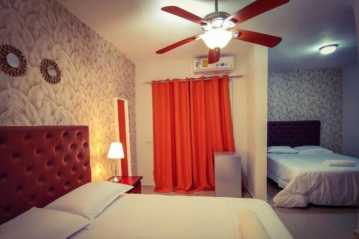 A hotel room with a tufted headboard, a ceiling fan, an air conditioning unit, a red curtain, and a bed with white linens.