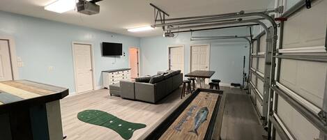 A room with a pool table, a sofa, a TV, and a garage door.