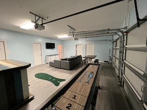 A room with a pool table, a sofa, a TV, and a garage door.