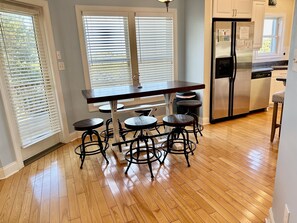 A kitchen with a wooden table and four stools, a stainless steel refrigerator, and white cabinets. - Holy Mackerel -Gorgeous, large home -Ocean view & Sound view -Great for families (Emerald Isle)