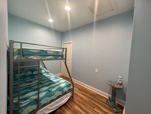A bunk bed with a blue ocean-themed bedspread, a small side table with a decorative item, and a wooden floor. - Holy Mackerel -Gorgeous, large home -Ocean view & Sound view -Great for families (Emerald Isle)