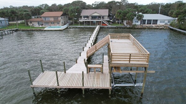 A wooden dock extending into a body of water with a house in the background. - Waterfront (Merritt Island)