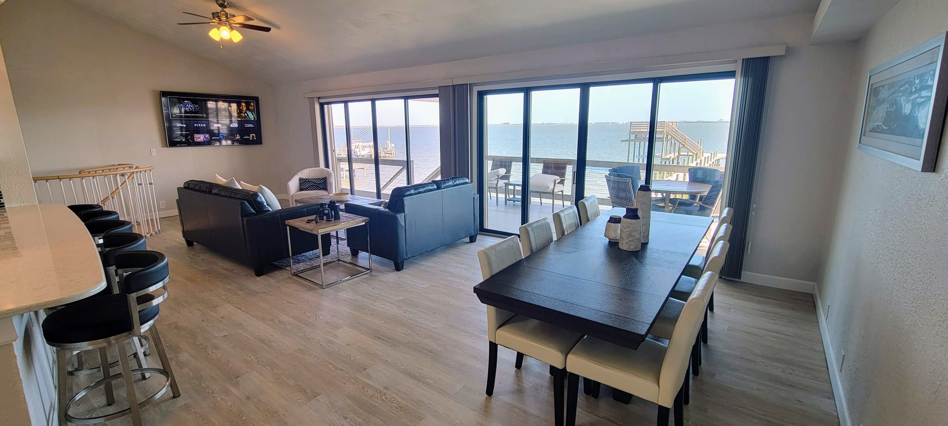 Un vaste espace de vie comprenant une grande fenêtre donnant sur la mer, une table à manger et un coin salon avec un canapé et des fauteuils.
