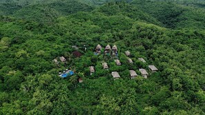 An aerial view of a resort with multiple thatched-roof cottages surrounded by dense forest. - BB Resort Villa and Spa (Penida Island)