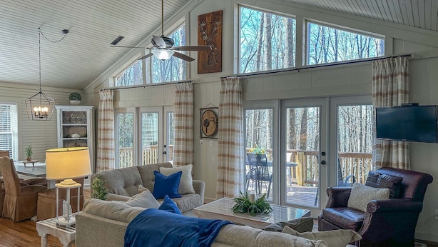 A spacious living room with a high ceiling, large windows, a ceiling fan, and a television. - Sky Valley Creekside Getaway! Hike-Swim-Golf! (Sky Valley)