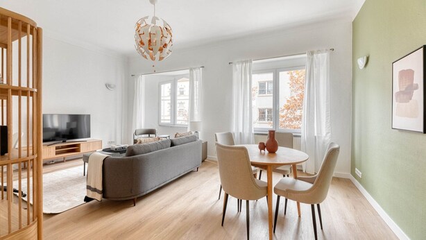 Ein modernes Wohnzimmer mit grauem Sofa, einem HolztV-Möbel und einem Essbereich mit rundem Tisch und Stühlen.