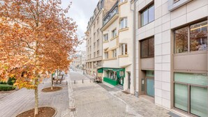 Eine moderne Stadtstraße mit Baumallee, einem Café und einem Gebäude mit großen Fenstern.