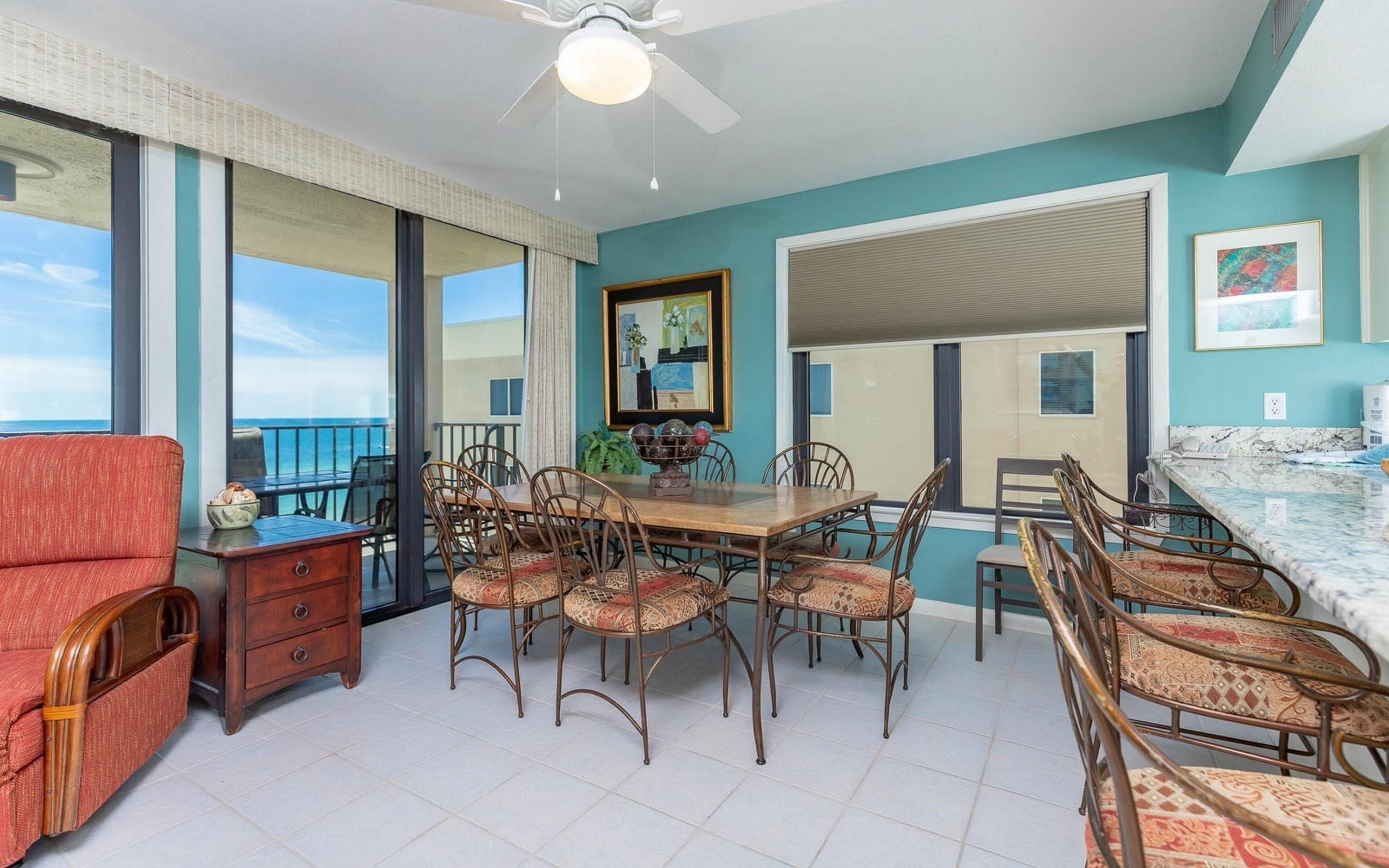 A spacious room with a dining table and chairs, a red armchair, a wooden dresser, and a ceiling fan.