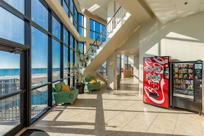 A spacious indoor area with large windows, a Coca-Cola vending machine, and a staircase leading to an upper level. - Phoenix I by Brett Robinson Vacations (Orange Beach)