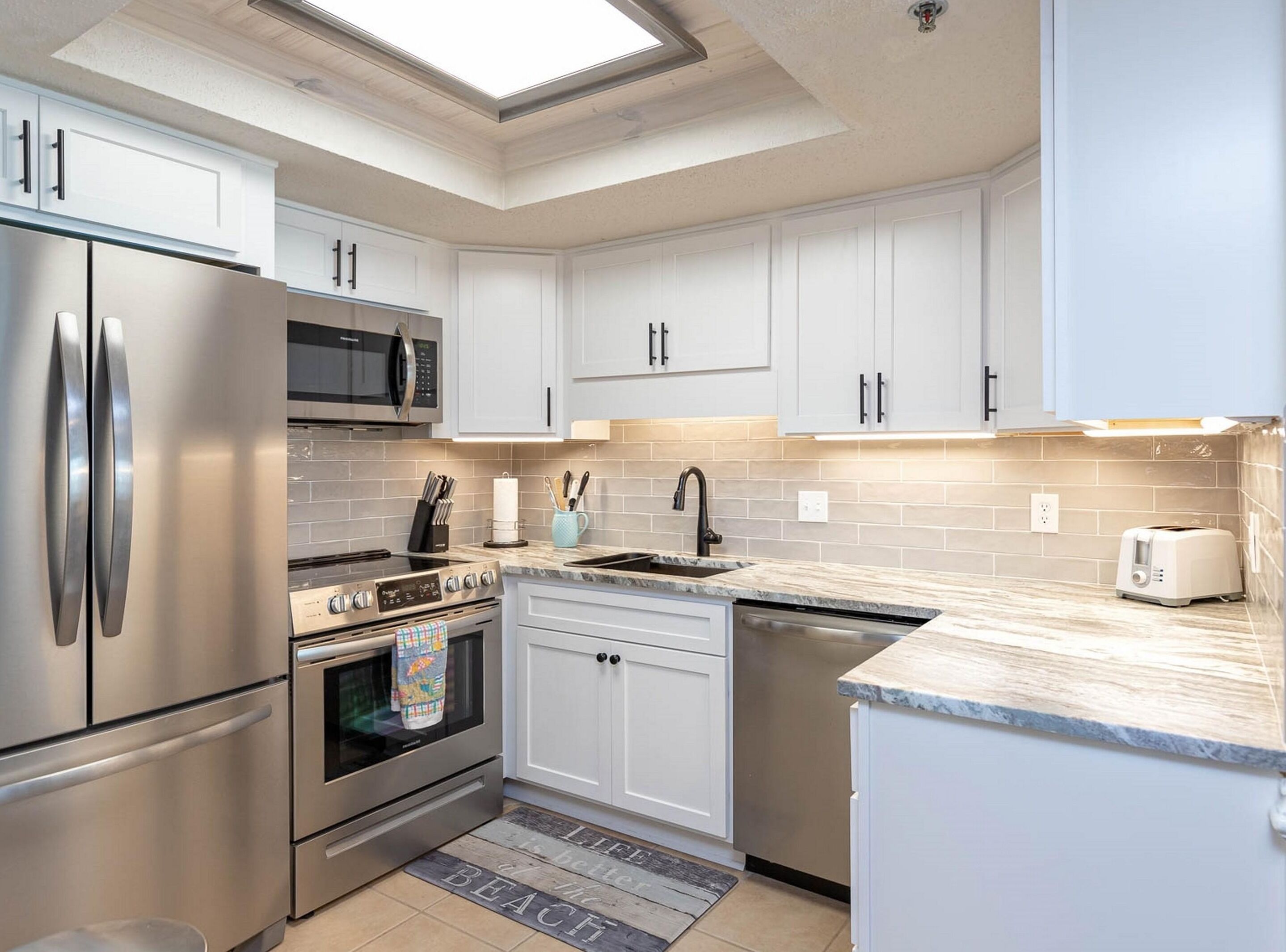 A modern kitchen with stainless steel appliances, white cabinetry, and a skylight.