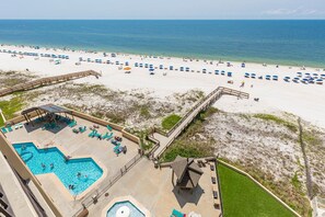 A beach resort with a pool area, beach umbrellas, and a boardwalk leading to the beach.