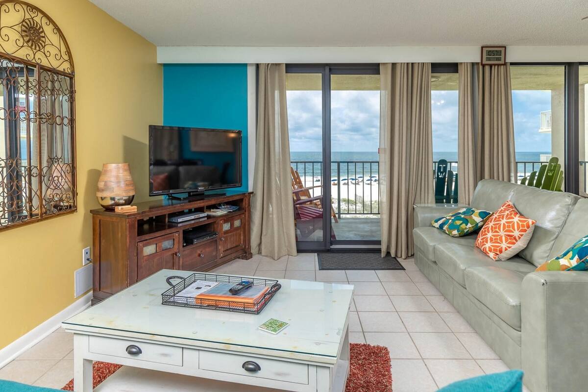 Un salon équipé d’un téléviseur, d’un canapé et d’un balcon offrant une vue sur la plage.