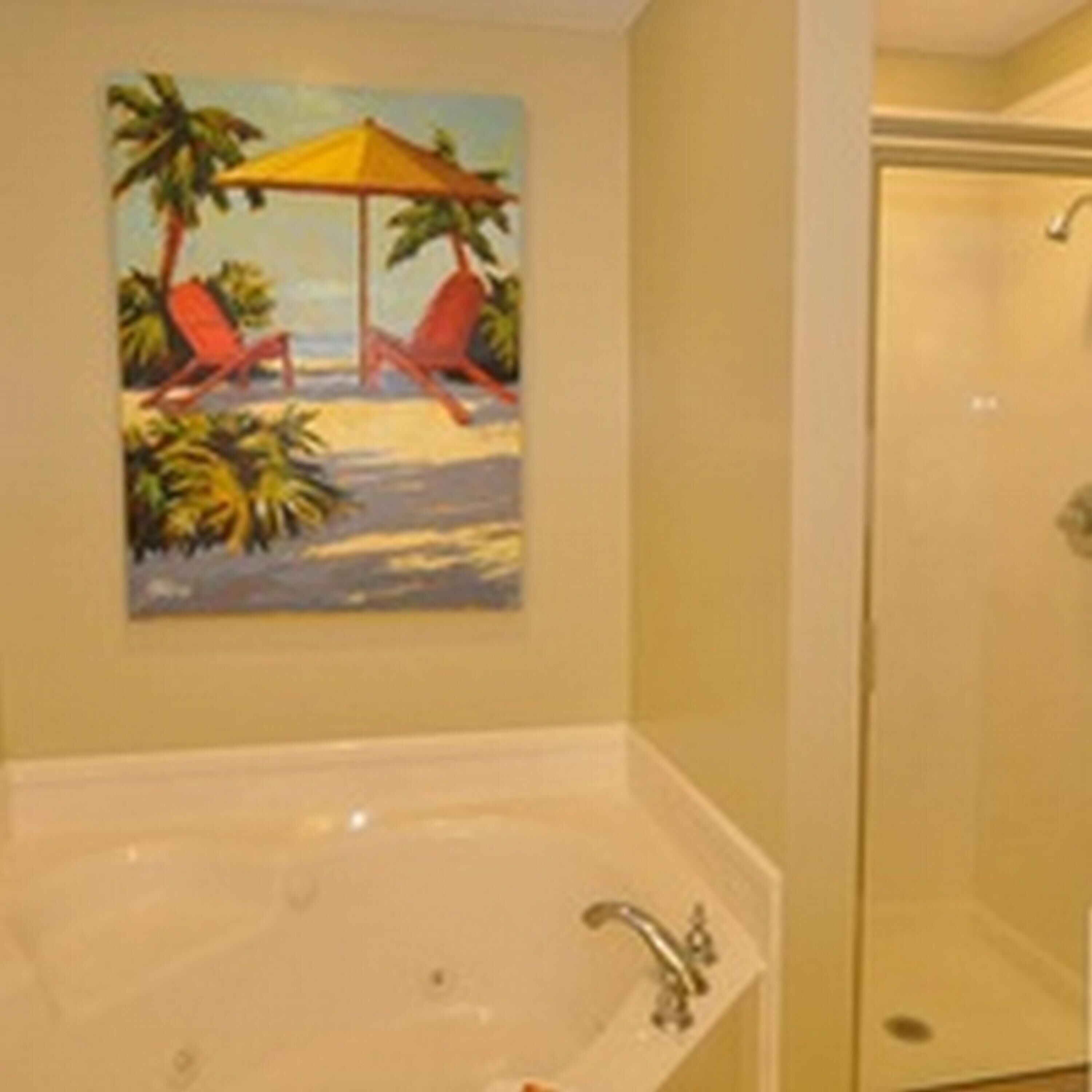 A bathroom with a large bathtub, a shower, and a painting of a beach scene.