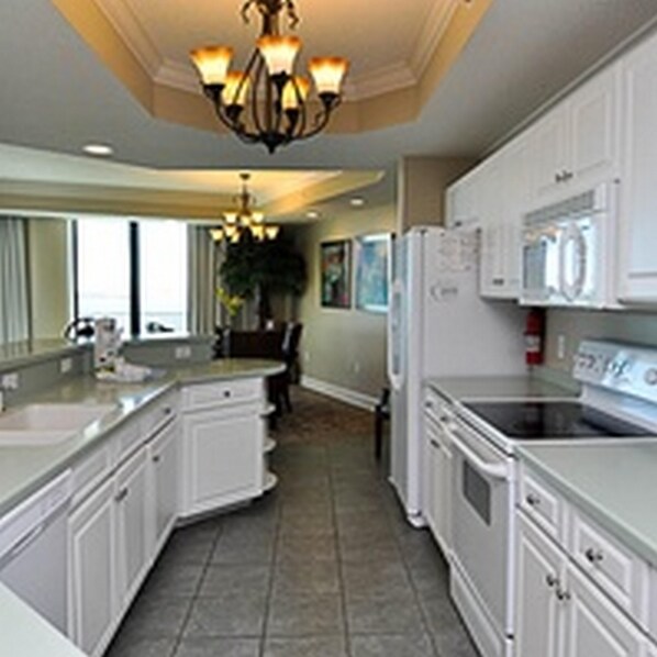 A kitchen with white cabinets, a central island, a chandelier, and a refrigerator.