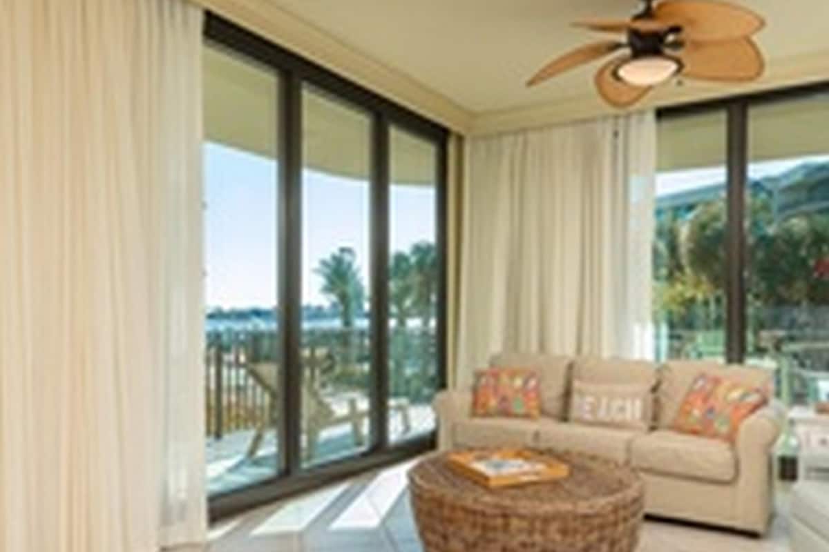 Un salon spacieux doté d’une grande fenêtre, d’un ventilateur de plafond et d’un coin salon confortable.