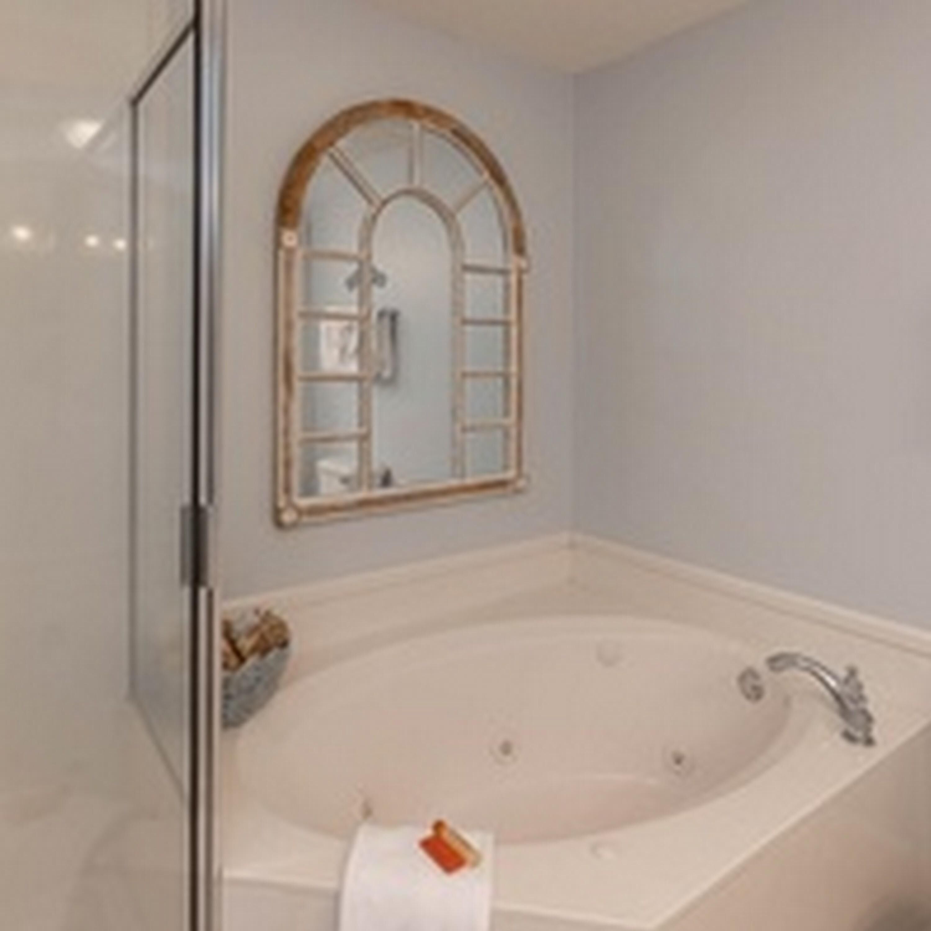 A bathroom with a freestanding bathtub, a mirror with a wooden frame, and a glass shower enclosure.