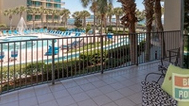 Un balcon d’hôtel donnant sur une piscine et des palmiers.