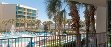 Un balcón de hotel con vista a una piscina y palmeras.