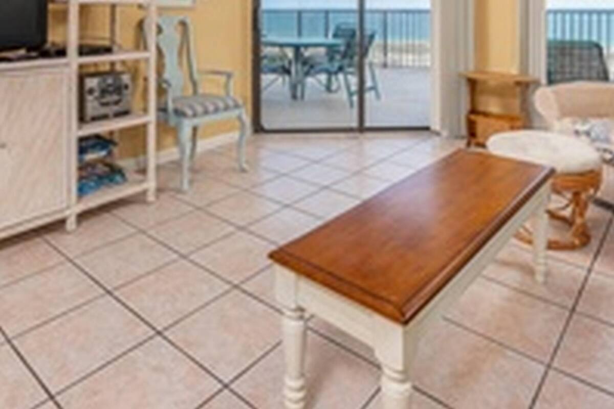 Habitación de hotel con una mesa de madera, un televisor en un mueble bajo, una estantería y un balcón con vista al mar.