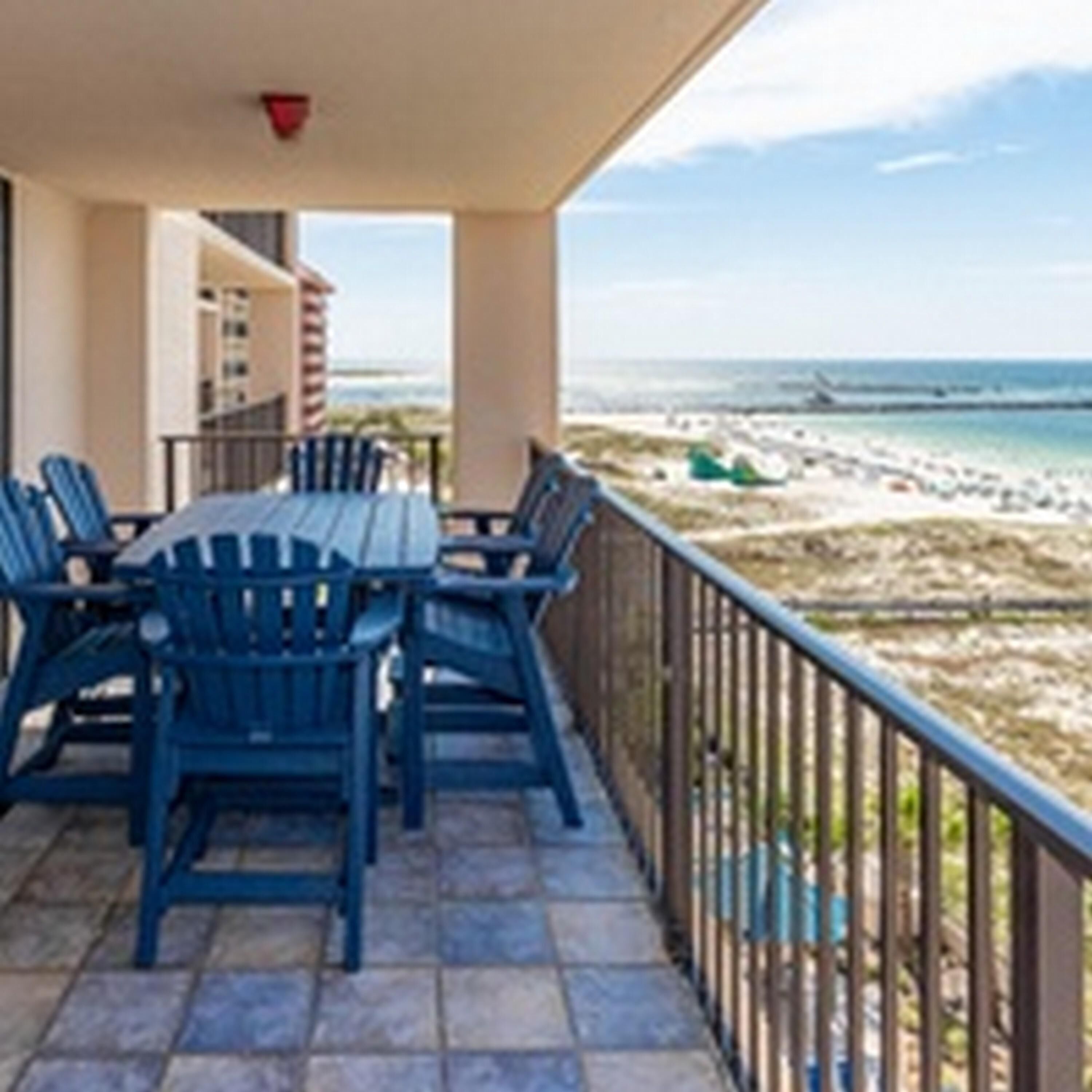 A balcony with a table and chairs, overlooking a beach and ocean.
