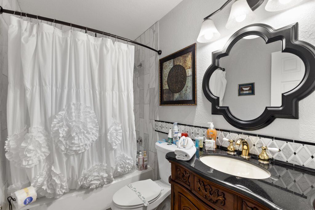 A bathroom with a white toilet, a sink with gold faucets, a shower curtain, and a mirror with a decorative frame.