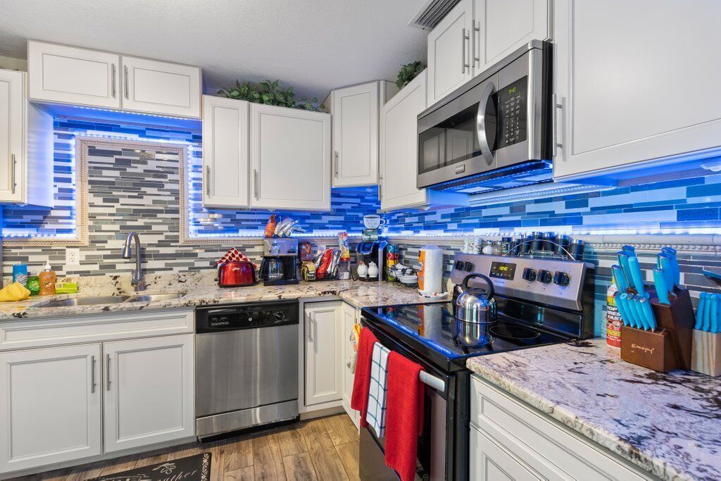 Una cocina moderna con armarios blancos, un lavavajillas de acero inoxidable, un microondas y una estufa.