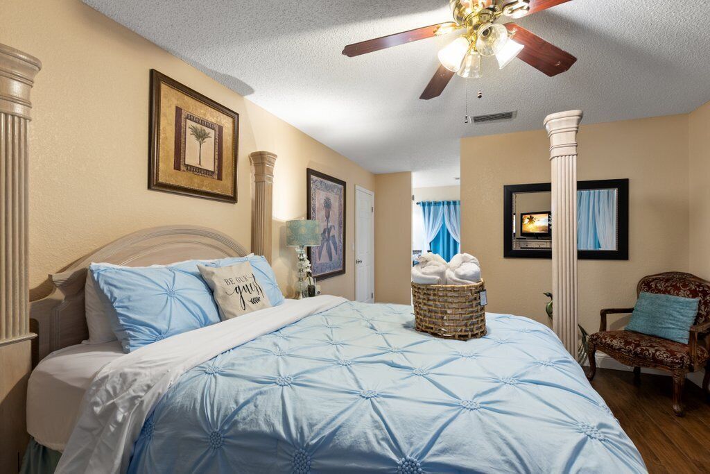A bedroom with a large bed, a ceiling fan, and a wicker basket with towels.